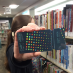 Staff person holding up a Cary Area Library card toward the camera.