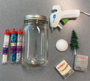 A photo of glitter tubes, mason jar, glue gun, styrofoam ball, polymer clay, and evergreen tree cupcake topper.