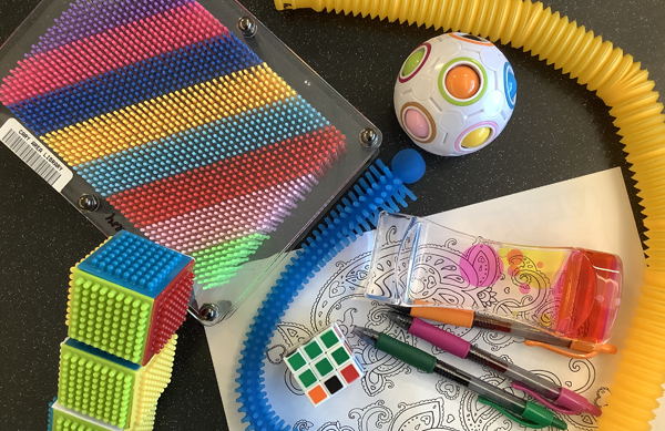 Photo of various things included in the Serenity Box, such as blocks, coloring pages and markers, fidget toys, and more.