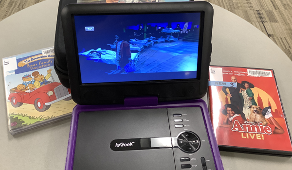 Photo of the portable DVD player with the screen open and playing a movie. DVD cases surround the player.