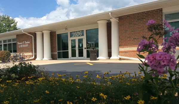 Photo of the front of the Library entrance with yellow and purple flowers in the foreground.