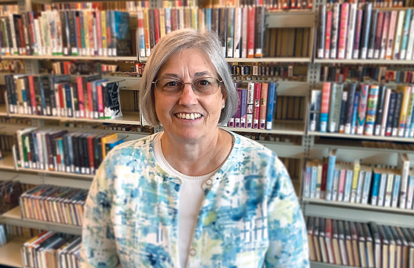 Photo of Diane McNulty, standing in front of shelves in the Library.