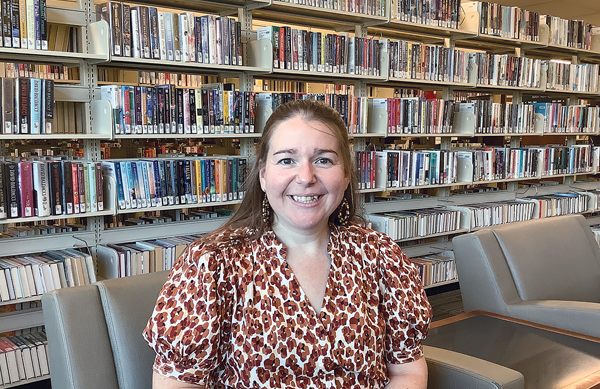 Photo of Mona Reynolds sitting in front of book shelves in the Library.