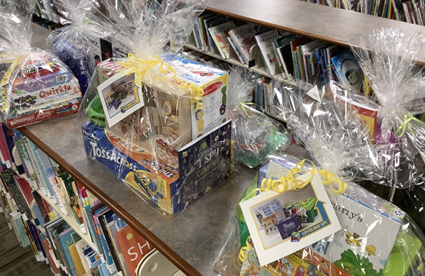 Overhead of grand prize packs for children, wrapped in cellophane and sitting on a picture book shelf.